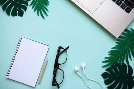 Workspace in a trendy blue color. Many different items including a laptop, glasses, notebook, and headphones are on the table.の写真素材