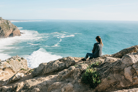 The girl at the top of the cliff in solitude admires the beautiful view of the Atlantic Ocean.の写真素材