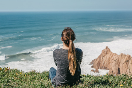 The girl at the top of the cliff in solitude admires the beautiful view of the Atlantic Ocean.の写真素材