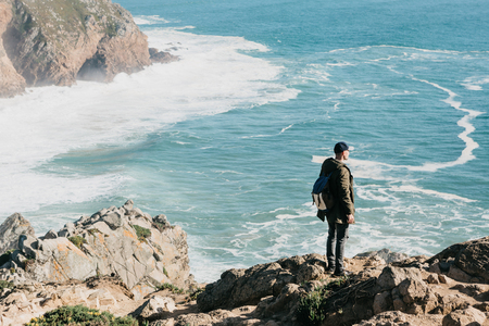 A man tourist with a backpack stands in solitude at Cape Roca in Portugal and enjoys a beautiful view of the Atlantic Ocean.の写真素材