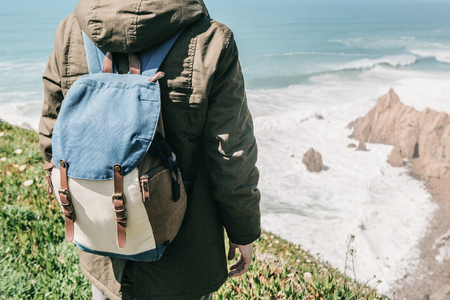 A man tourist with a backpack stands in solitude at Cape Roca in Portugal and enjoys a beautiful view of the Atlantic Ocean.の写真素材