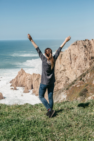 The girl next to the Atlantic Ocean in Portugal raises up her hands shows how pleased she is.の写真素材
