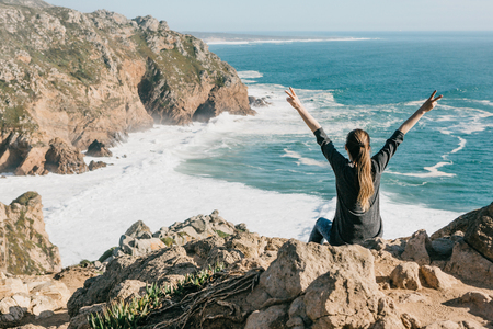 The girl next to the Atlantic Ocean in Portugal raises up her hands shows how pleased she is.の写真素材