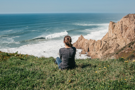The girl at the top of the cliff in solitude admires the beautiful view of the Atlantic Ocean.の写真素材
