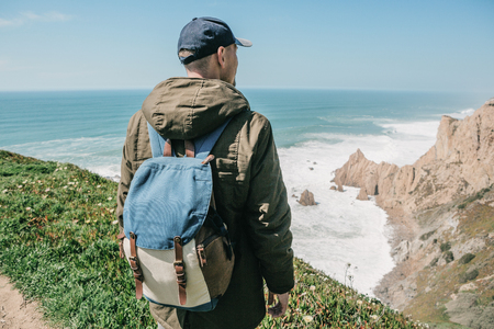 A man tourist with a backpack stands in solitude at Cape Roca in Portugal and enjoys a beautiful view of the Atlantic Ocean.の写真素材