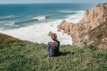 The girl at the top of the cliff in solitude admires the beautiful view of the Atlantic Ocean.の写真素材