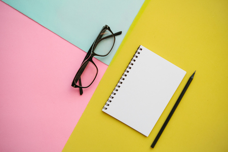 Notepad, glasses and a pencil on a multi-colored background.の写真素材