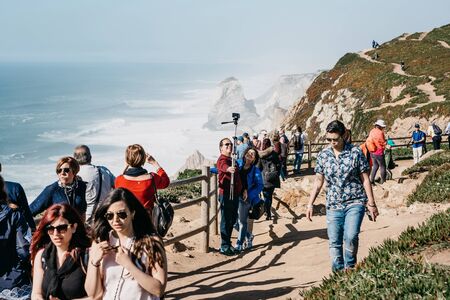 Portugal, Sintra, June 26, 2018: A group of people or tourists admire sights and take pictures and take selfies at Cape Roca.のeditorial素材