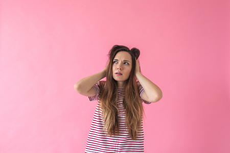 A portrait on a pink background of a girl who thinks about something or solves some problem in her mind.の写真素材