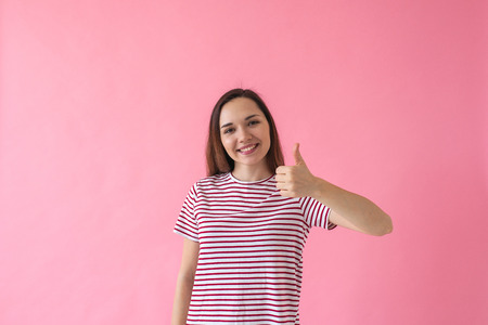Positive smiling girl on a pink background shows fingers gesture meaning Like or Ok.の写真素材