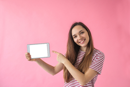 A girl holds in her hand a tablet with a blank screen on a pink background.の写真素材