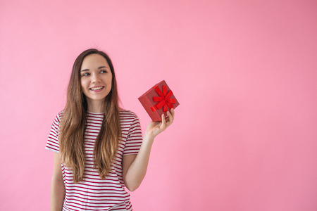Smiling cute girl holds in her hand a box with a gift on a pink background.の写真素材