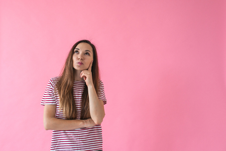 Portrait on a pink trendy background of a girl who is thinking or dreaming about something.の写真素材
