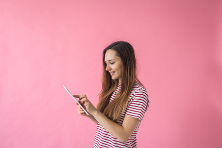 Cute young girl using tablet on a pink background.の写真素材