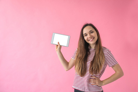 A girl holds in her hand a tablet with a blank screen on a pink background.の写真素材
