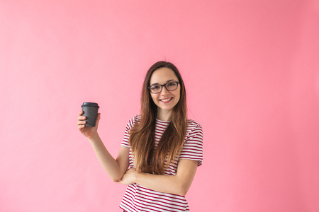 Beautiful smiling positive girl drinks coffee on a pink background. Coffee break.の写真素材