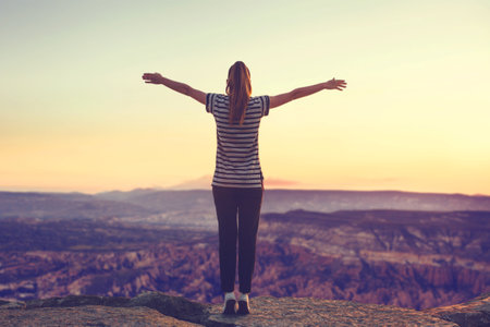 The girl at the top of the mountain alone, admires the beautiful view of the natural landscape and raises her hands up.の写真素材