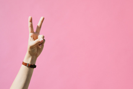 Girl shows peace sign on a pink background.の写真素材