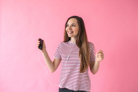 Positive joyful girl on a pink background listening to music.の写真素材