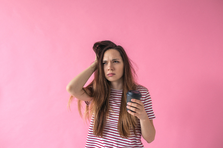 Sleepy girl with wild hair and coffee in hand on a pink background. She cant wake up.の写真素材