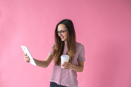 Cute young girl using tablet on a pink background.の写真素材