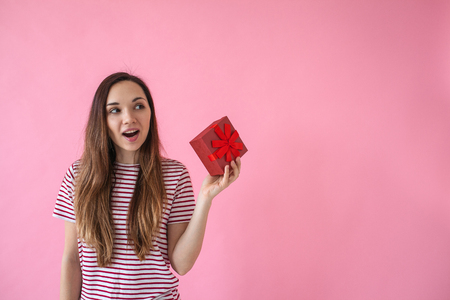 Surprised girl holds in her hand a box with a gift on a pink background.の写真素材