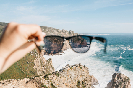Person holds sunglasses on the background of the Atlantic Ocean. Selective focus on the ocean. Recreation concept.の写真素材