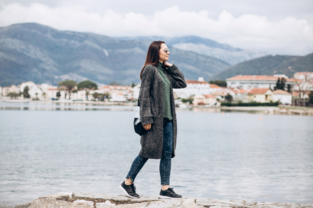 Beautiful young trendy girl walks near the sea against the backdrop of Tivat in Montenegro.の写真素材