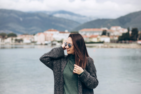 Beautiful young trendy girl in sunglasses walks near the shore and looks into the distance.の写真素材