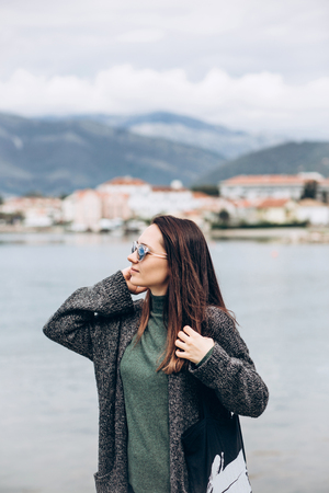 Beautiful young trendy girl in sunglasses walks near the shore and looks into the distance.の写真素材