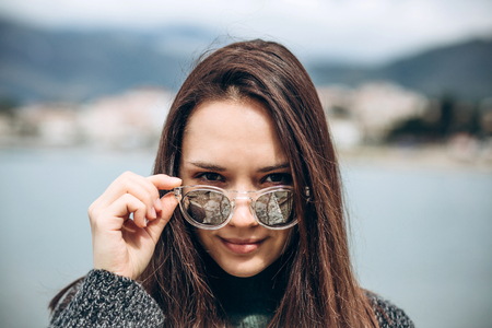 Portrait of a beautiful young fashionable girl on the background of the sea and the coastal city.の写真素材