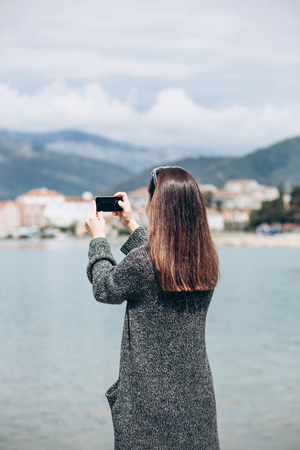 A girl or a tourist photographs a beautiful view of the sea and the urban architecture of the small coastal town of Tivat in Montenegro.の写真素材