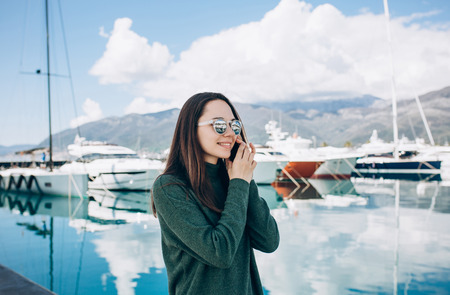 Beautiful girl talking on a cell phone on the background of yachts in the port of Porto Montenegro in Tivat in Montenegro.の写真素材