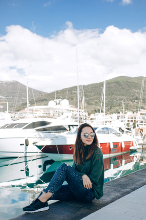 A beautiful young girl in sunglasses is sitting next to yachts in Porto Montenegro in Tivat in Montenegro.の写真素材