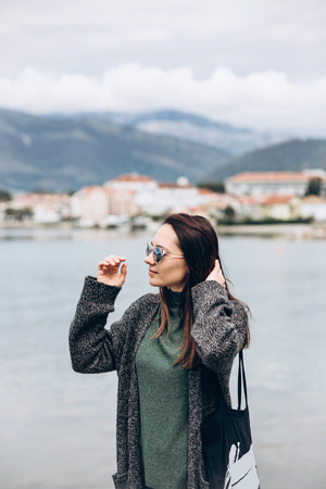 Beautiful young trendy girl in sunglasses walks near the shore and looks into the distance.の写真素材