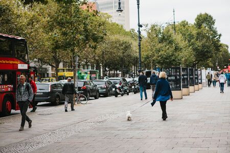 Berlin, October 1, 2017: City street with people and cars. Normal city life. A woman walking a dog,...