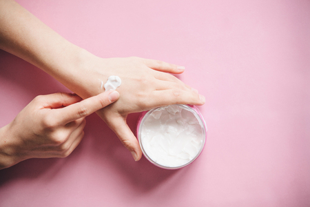 Female hands with cream on a pink background in minimal style. Skin care, beauty and health.の写真素材