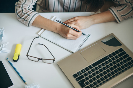A young beautiful student girl does homework or writes a to-do list or this girl works in a home office. Home education or business or planning.の写真素材