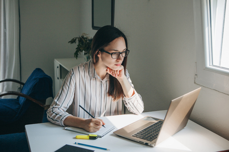 A young beautiful student girl does homework or writes a to-do list or this girl works in a home office. Home education or business or planning.の写真素材