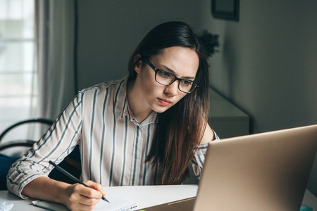 A young beautiful student girl does homework or writes a to-do list or this girl works in a home office. Home education or business or planning.の写真素材