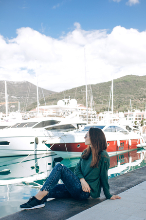 A beautiful young girl in sunglasses is sitting next to the yachts in Porto Montenegro in Tivat in Montenegro resting and looking at the yachts.の写真素材