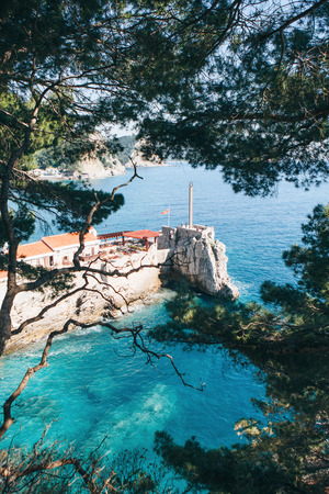 Beautiful view through the trees to the old fortress or bastion among the sea in Petrovac in Montenegro. Popular tourist destination.の写真素材