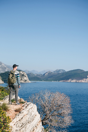 A tourist with a backpack on top of a cliff or hill next to the sea looks into the distance. Travel alone.の写真素材