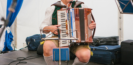 An accordionist in traditional Bavarian clothes plays the accordion on the stage. The accordionist plays the musical instrument.の写真素材