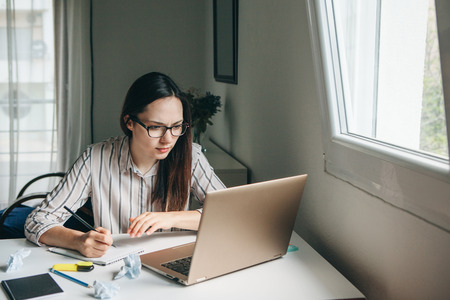 A young beautiful student girl does homework or writes a to-do list or this girl works in a home office. Home education or business or planning.の写真素材