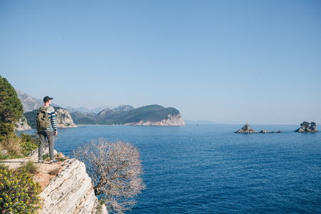 A tourist with a backpack on top of a cliff or hill next to the sea looks into the distance. Travel alone.の写真素材