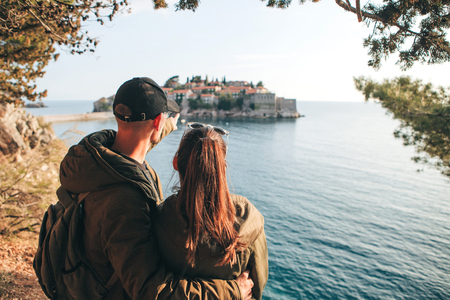 A young couple of tourists admires the beautiful view of the sea and the island of Sveti Stefan in Montenegro.の写真素材