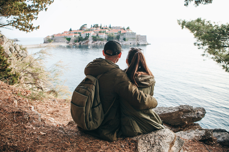 A young couple of tourists admires the beautiful view of the sea and the island of Sveti Stefan in Montenegro.の写真素材
