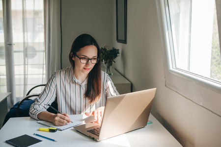 A young beautiful student girl does homework or writes a to-do list or this girl works in a home office. Home education or business or planning.の写真素材