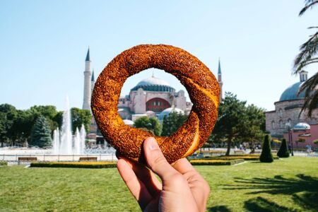 The person is holding a traditional Turkish fast food bagel called Simit against the background of...